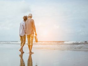 A senior couple walking on a beach at sunset while holding hands